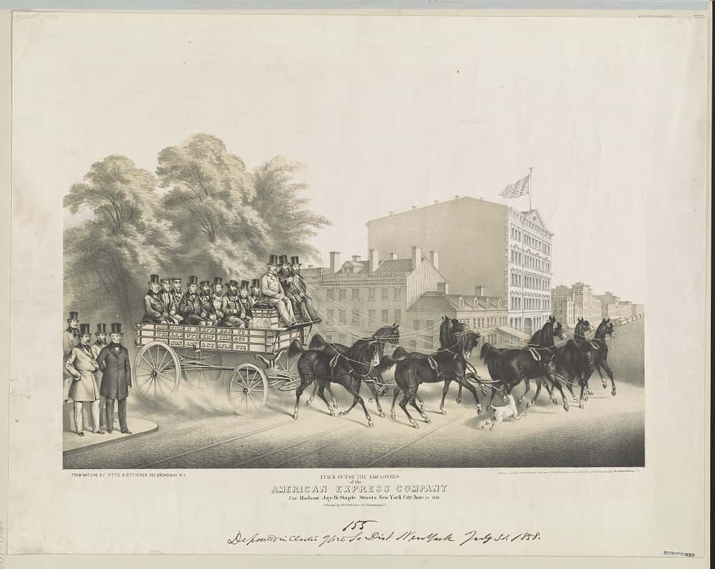 People are seen in a horse-drawn carriage as well as people in front on a city street in New York with buildings and trees.