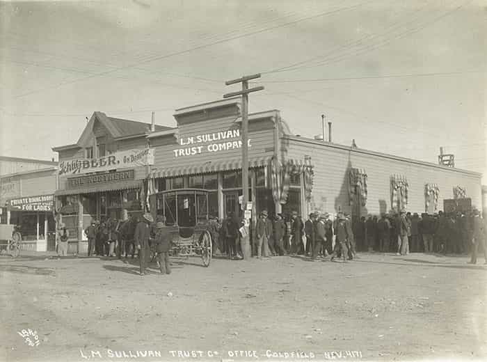 Black and white photograph of the front of the L.M. Sullivan Trust building with crowds of people around it.